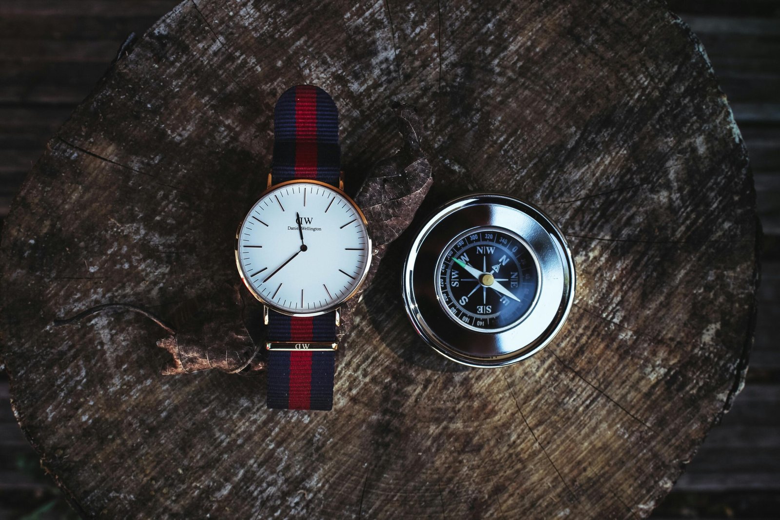 A wristwatch and a compass placed on a wooden stump, captured from above.